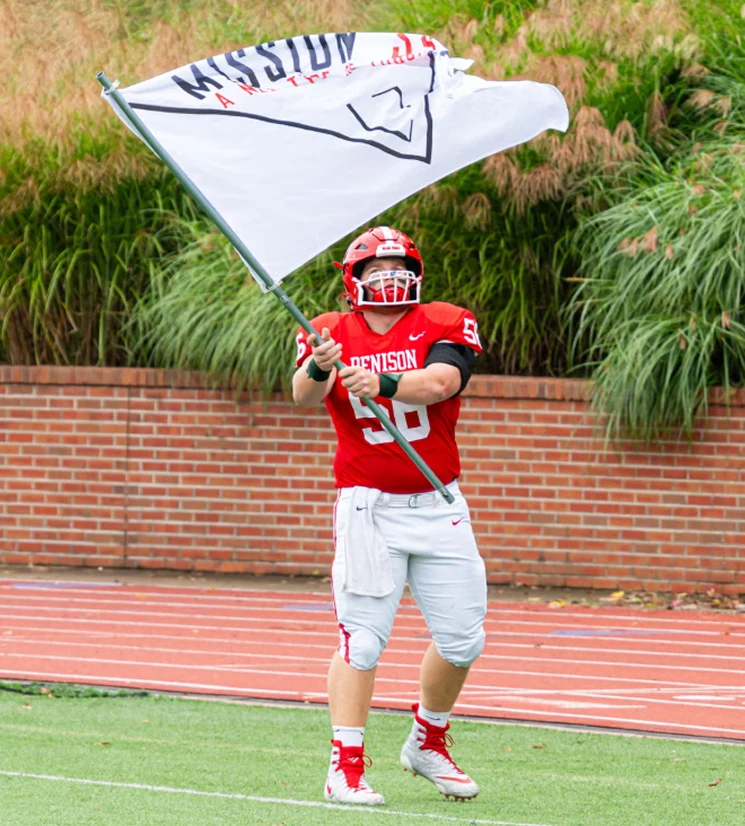 Canyon Schneider carrying the Mission 34 flag onto the field at Denison